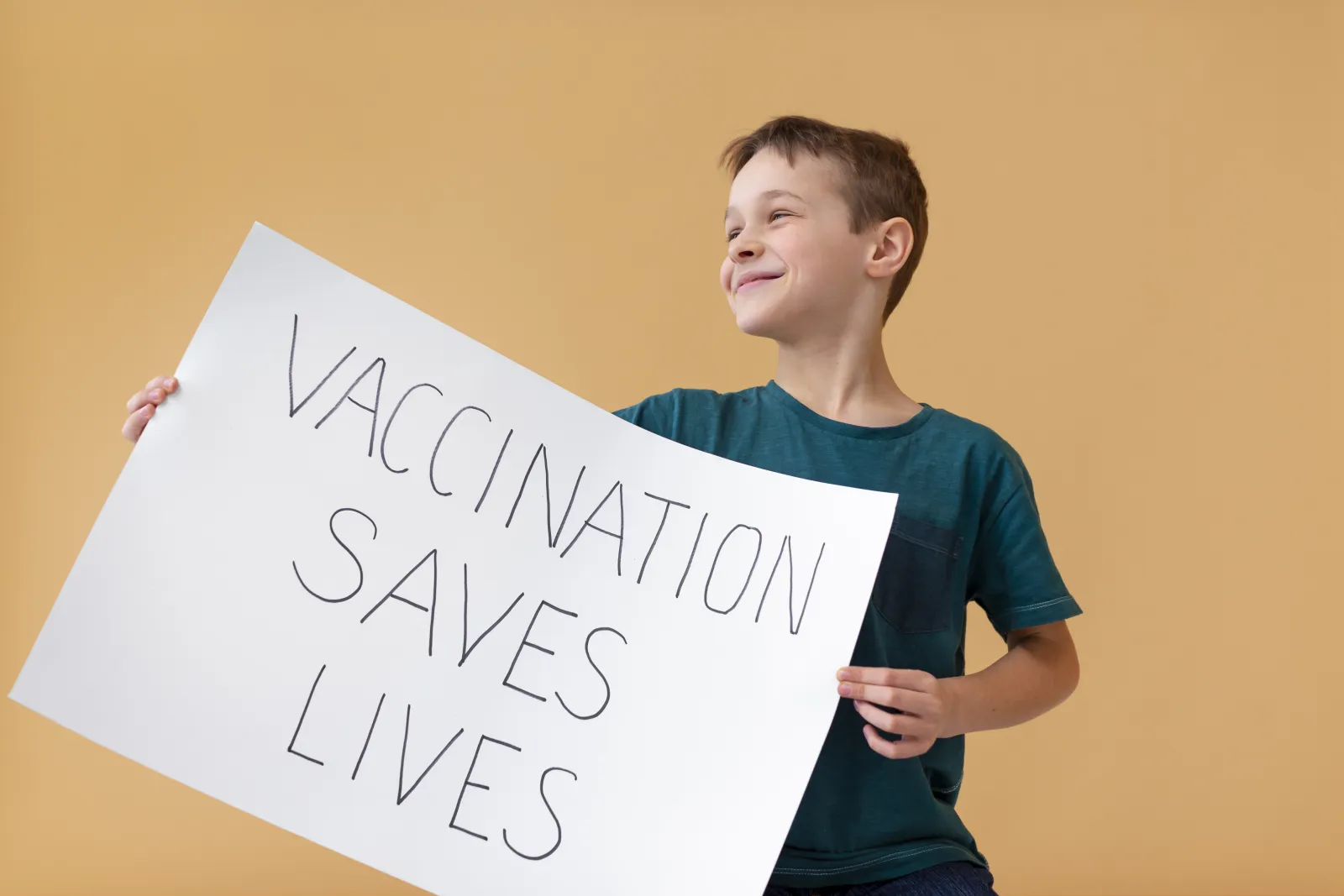 Un collégien souriant tenant une pancarte « Vaccination saves lives »
